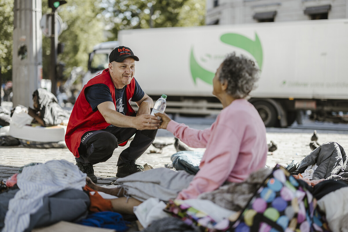 Dimitri Boclaci, salarié à l'Armée du Salut, tend une bouteille d'eau à une femme, lors d'une maraude dans les rues de la capitale, mardi 25 juin 2024.